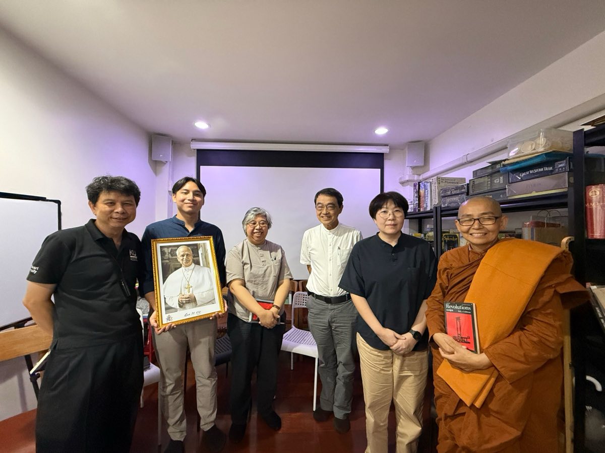 Six participants standing together after the dialogue, one holding a framed portrait of Pope Leo XIV, a bhikkhuni at the right holding a copy of Jack Goldstone's Revolutions.